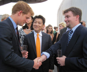 British Prince Harry (left) shakes hands with U.S. Marine Corporal Joshua Maloney (right), while W.P. Andrew Lee looks on. Lee, a professor of surgery and orthopedic surgery as well as chief of the Division of Plastic Surgery in the University of Pittsburgh School of Medicine, performed the 2009 transplant that gave Maloney a new right hand. Maloney’s own hand had been destroyed during a 2007 military training exercise. The three men met in New York City during a June 25 reception that Prince Harry hosted on the aircraft carrier USS Intrepid to honor British and American veterans. The prince, who is training to become a pilot with the British Army Air Corps, is interested in Pitt and UPMC’s hand-transplantation program. He spoke with Lee and Maloney about the medical procedure and its potential to help other wounded warriors.  	  