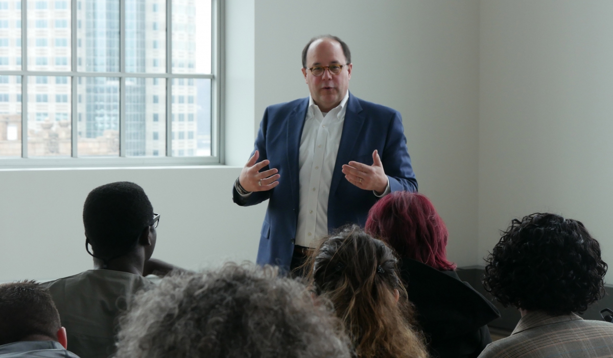 A middle-aged man lectures to a group of students.