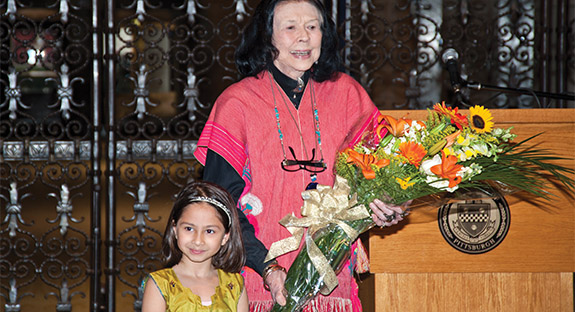 E. Maxine Bruhns celebrated her 50th anniversary as director of Pitt’s Nationality Rooms and Intercultural Exchange Programs during an Oct. 30 reception in the Cathedral of Learning’s Commons Room. Sponsored by the University Center for International Studies, more than 200 colleagues and supporters attended the event honoring the flamboyant and energetic Bruhns. The 30 Nationality and Heritage Rooms, representing the culture of ethnic groups that settled Allegheny County, are located in the Cathedral of Learning and are used as classrooms. Bruhns, who assumed her post in June 1965, has overseen the development of 11 rooms. Above, Bruhns accepts a bouquet alongside Alessia Raman, daughter of Veronica Dristas, assistant director of outreach for Pitt’s Global Studies Center.  