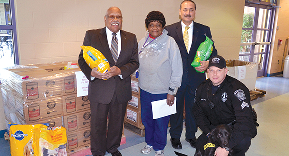 The Pitt Police Department’s two canines, Officers Riggs (four legs, bottom right) and Filo (exploring in nearby room) served as honorary cochairs of the Pitt’s People for Pets drive. Standing at Animal Friends, from left, are John Wilds, Pitt assistant vice chancellor for community relations; Eula Houston, Animal Friends’ animal care and enrichment coordinator; and Kannu Sahni, director of community relations, Pitt’s Office of Community and Governmental Relations. Kneeling is Pitt Police Officer David Nanz, who is Officer Rigg’s partner. Not pictured is Corey Rodgers, partner of K-9 Officer Filo.